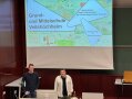Präsentation des Planes der Studierenden mit Thema "Posie der abgerundeten Ecken" - im Hintergrund gemalte Bilder von Grundschülern