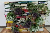 Bücher sind gestapelt und bilden einen Bücherschrank. Aus den Nischen "wachsen" Blumen.